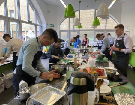 A diverse team of employees participating in a cookery class, illustrating teamwork and collaboration in a kitchen setting.